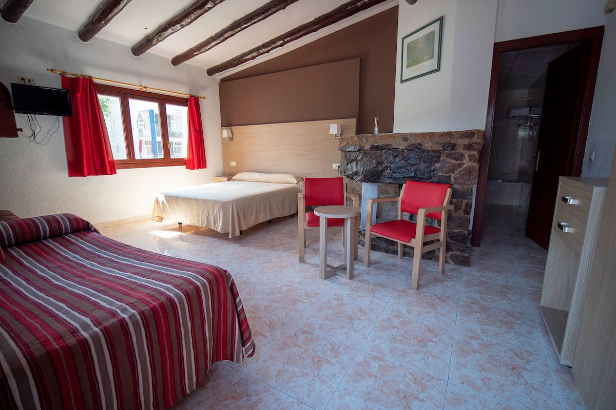 Un dormitorio con cama, escritorio, dos sillas, chimenea de piedra y televisor montado en la pared.