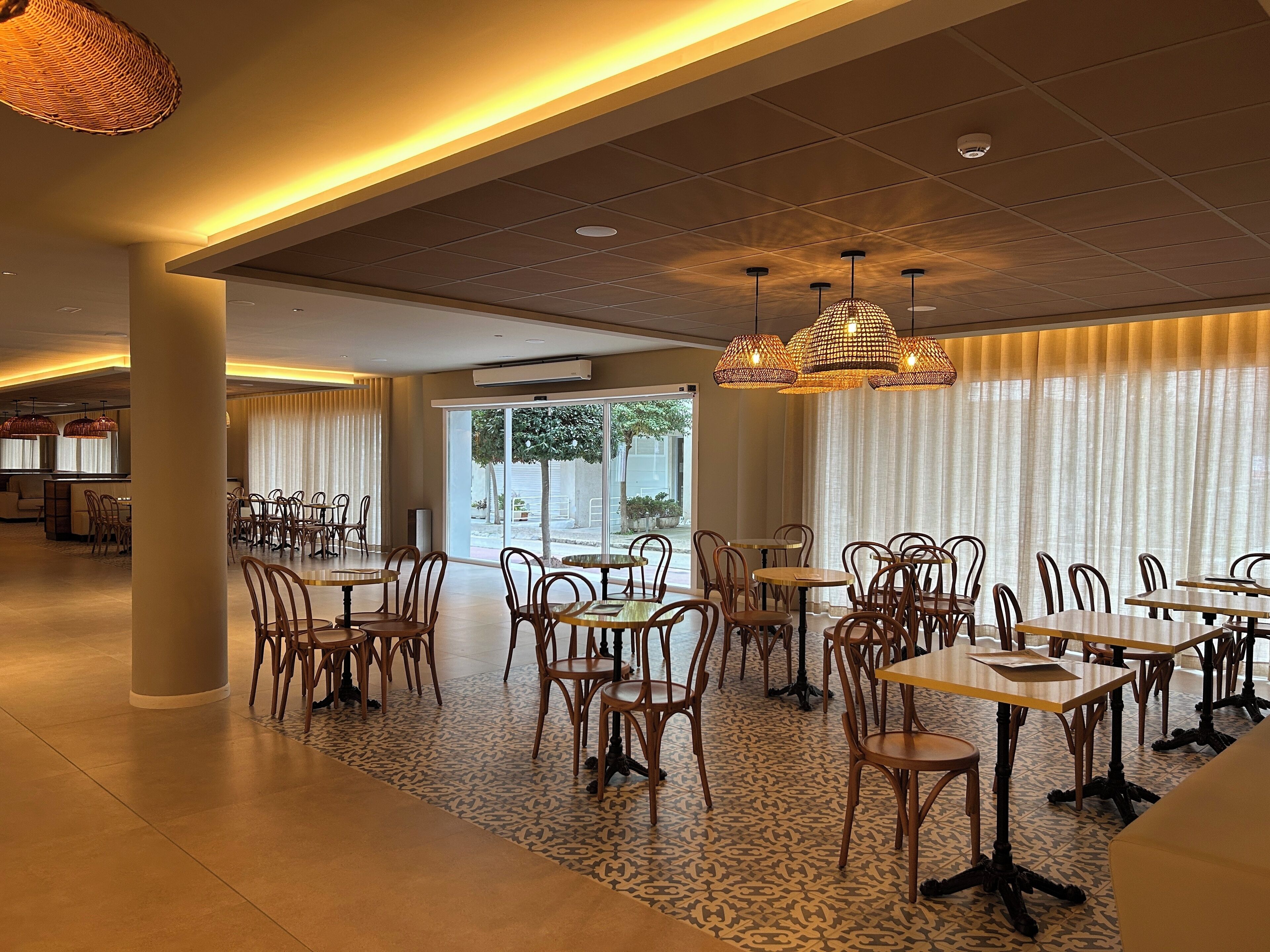 Un vaste espace dédié à la salle à manger, avec de nombreuses tables et chaises, de grandes fenêtres dotées de rideaux et un sol à motifs.