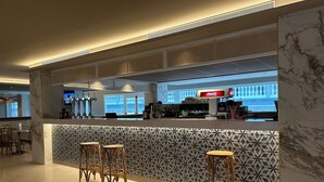 Een moderne barruimte met een patroonwand, barstoelen en een Coca-Cola koelkast.