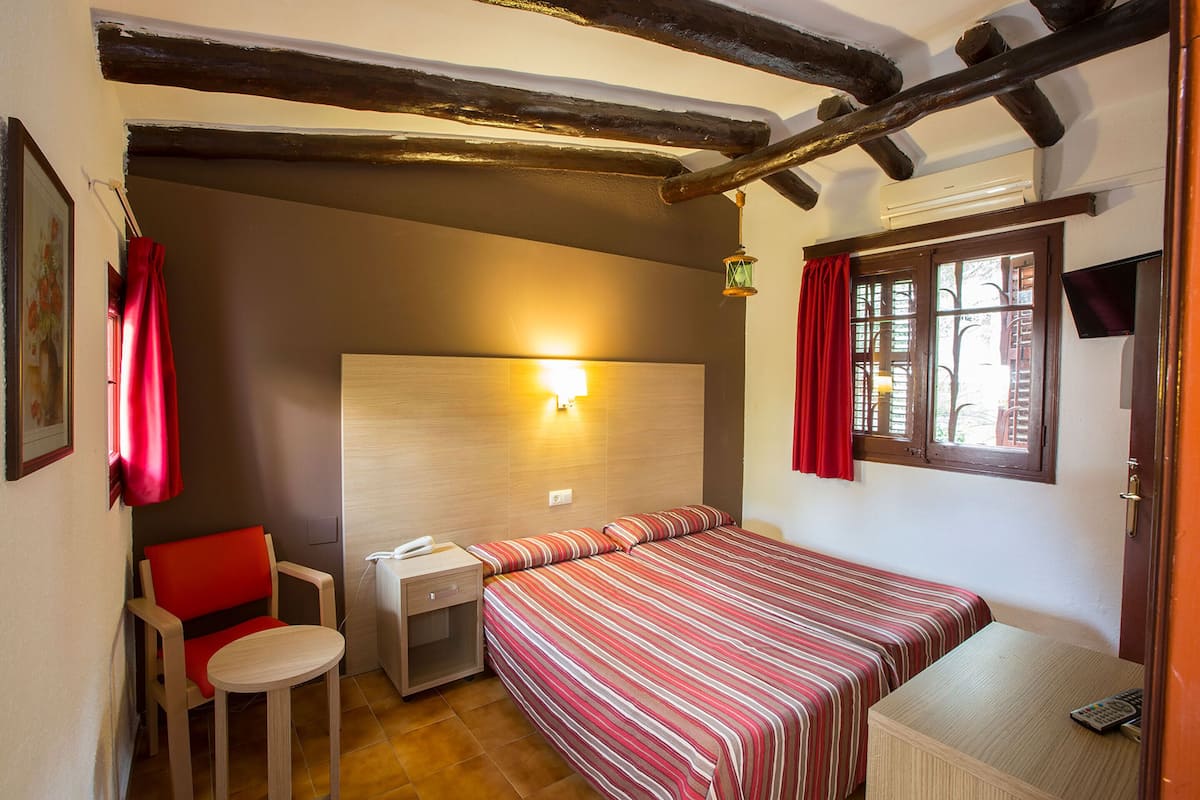 Una habitación pequeña y acogedora con cama, una silla, un escritorio y una ventana.