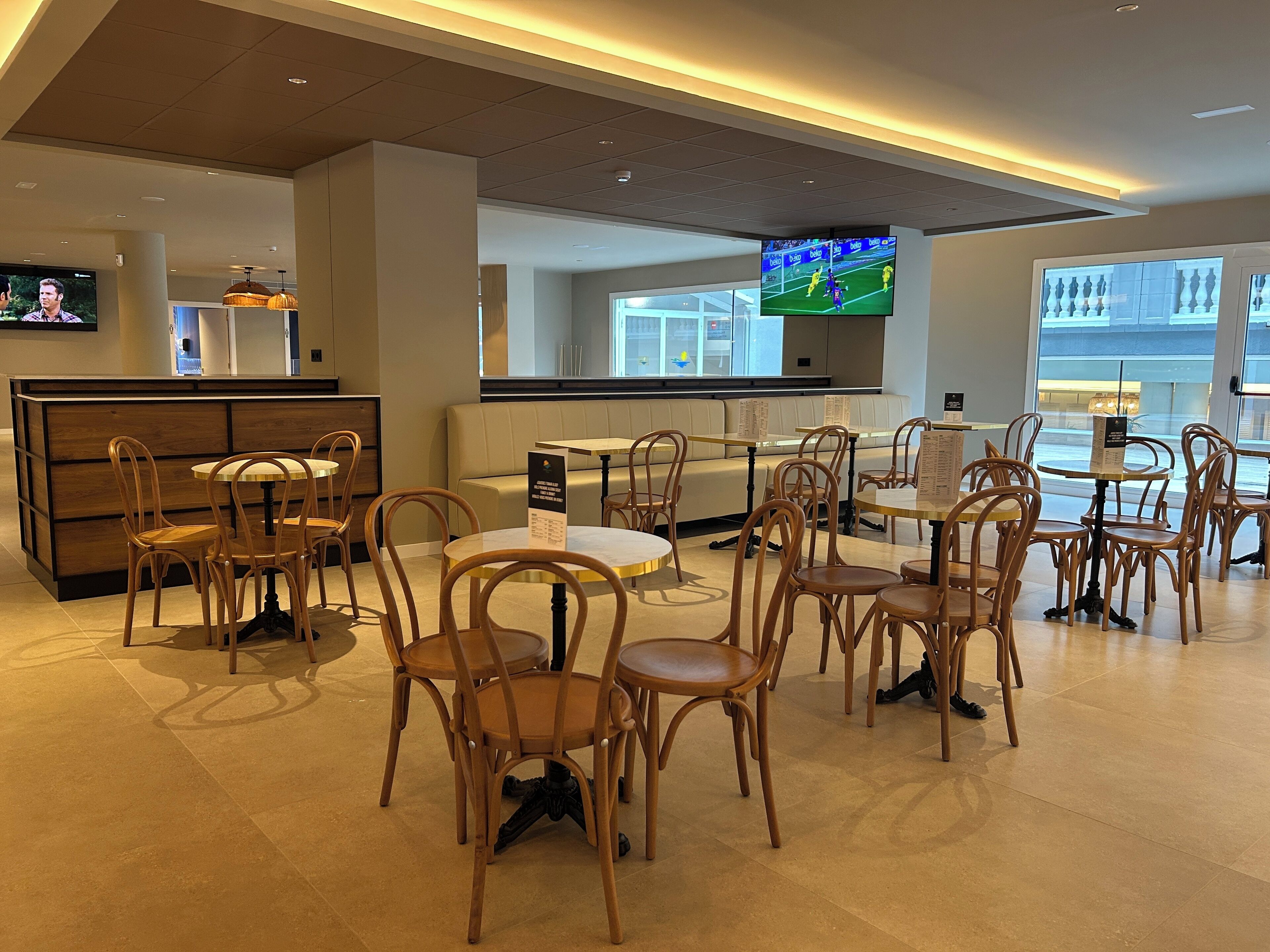 Un restaurant moderne avec des chaises et des tables en bois, un grand écran de télévision et un coin salon avec un canapé.