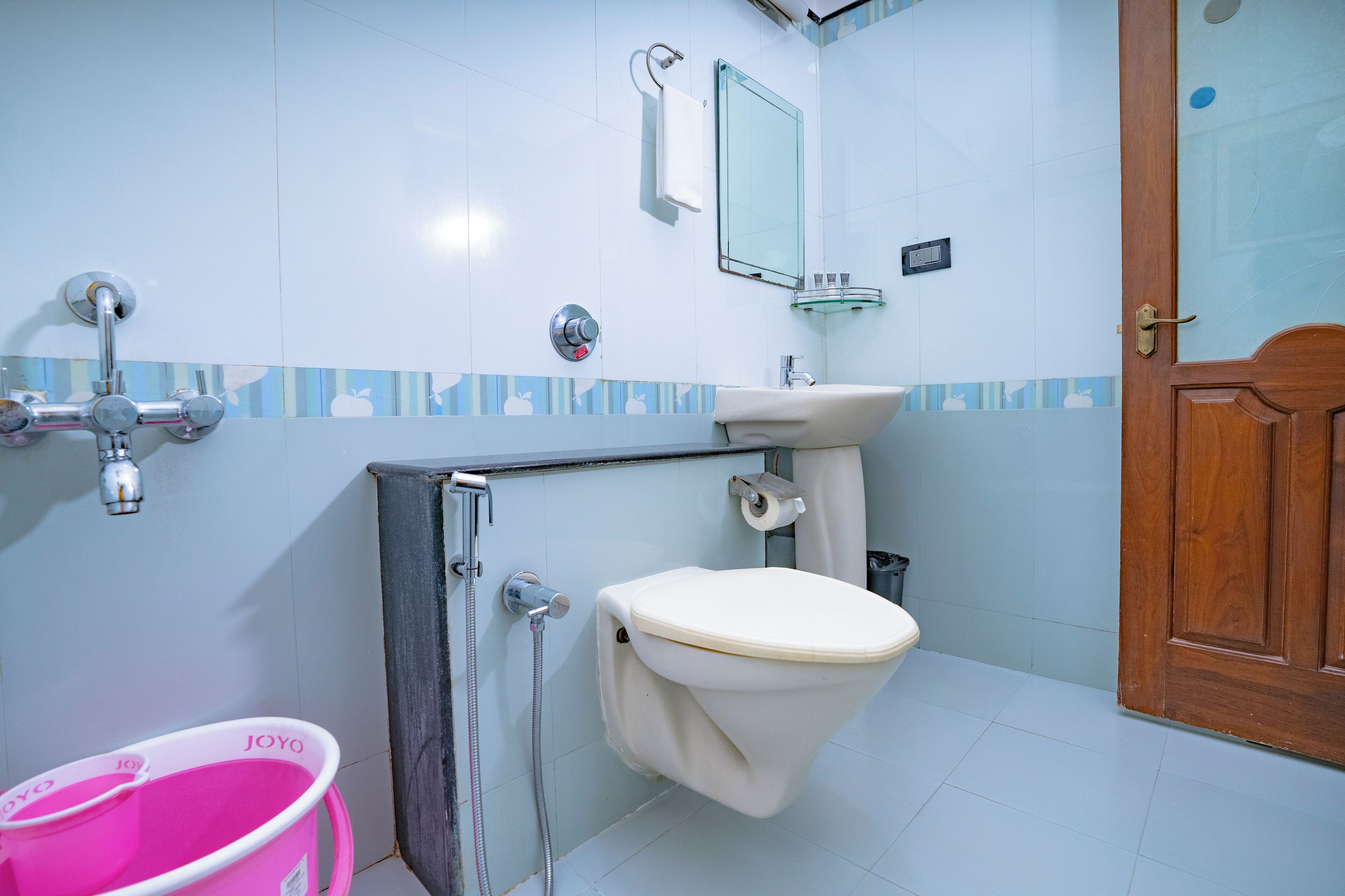 A bathroom with a toilet, sink, and shower. There is a pink bucket and a wooden door.