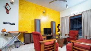 A living room with a yellow wall, a television, red chairs, and a glass coffee table. - SS Mystic Apartotel (Bengaluru)