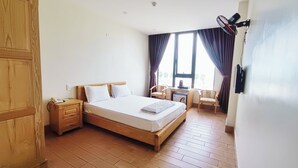 Habitación de hotel con cama de madera, escritorio con silla, una mesita y un ventilador.