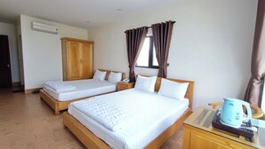 Habitación de hotel con dos camas individuales, cabeceros de madera, un armario, una mesita de noche con hervidor y una ventana con cortinas.