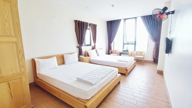 Habitación de hotel con dos camas de madera, una mesita, sillas y un ventanal con cortinas.