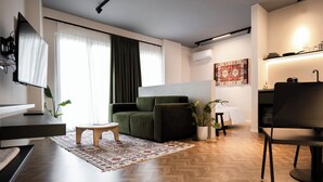 A modern living room with a green sofa, a small wooden table, and a herringbone wooden floor. - Muz Studios (Tirana)