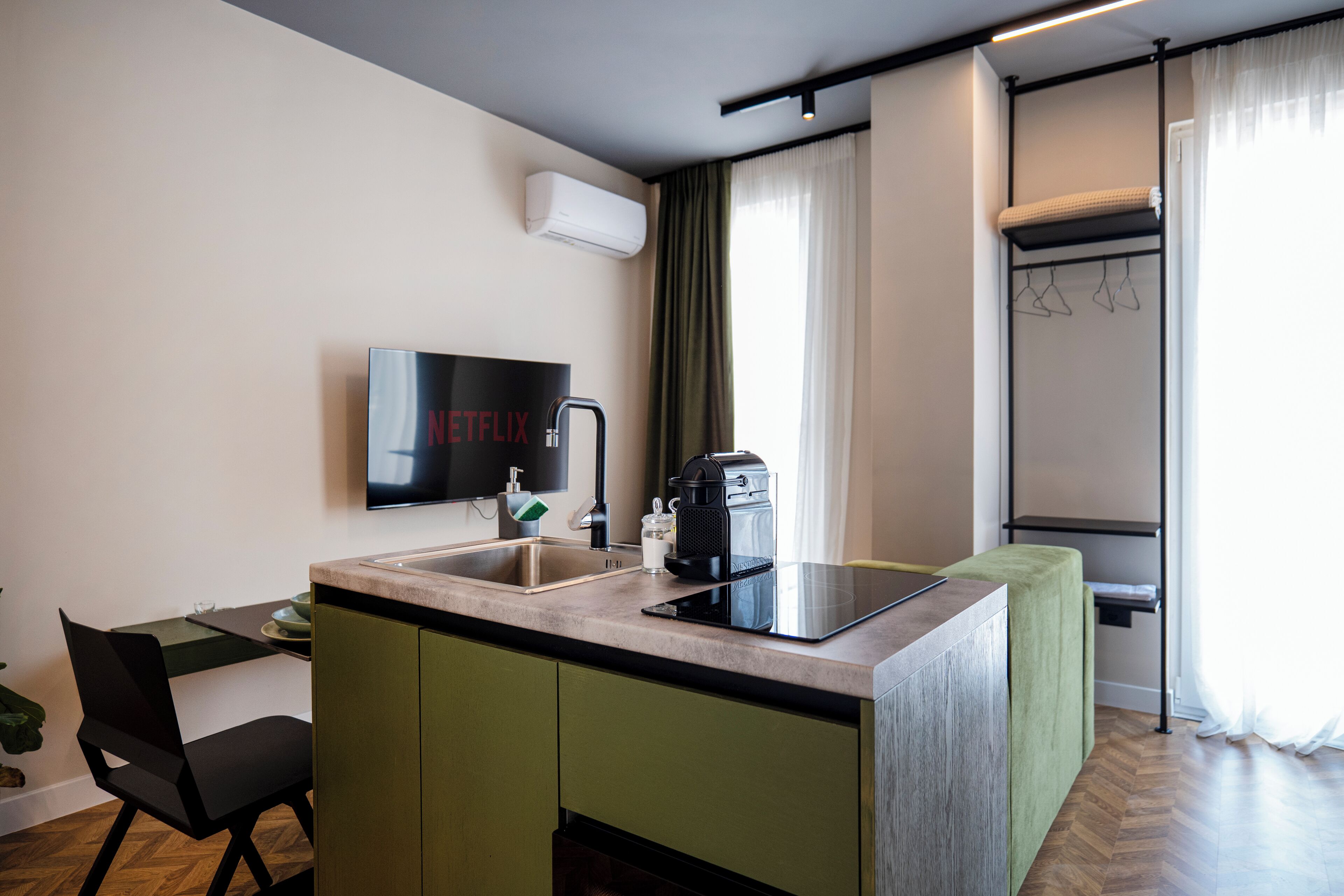 A modern kitchen with a built-in stove, sink, and a flat-screen TV mounted on the wall.