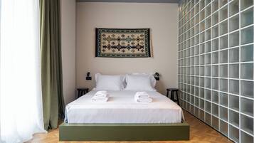 Una camera d'albergo moderna con un letto grande, una pedana verde, un arazzo appeso al muro e un'ampia finestra con tende.