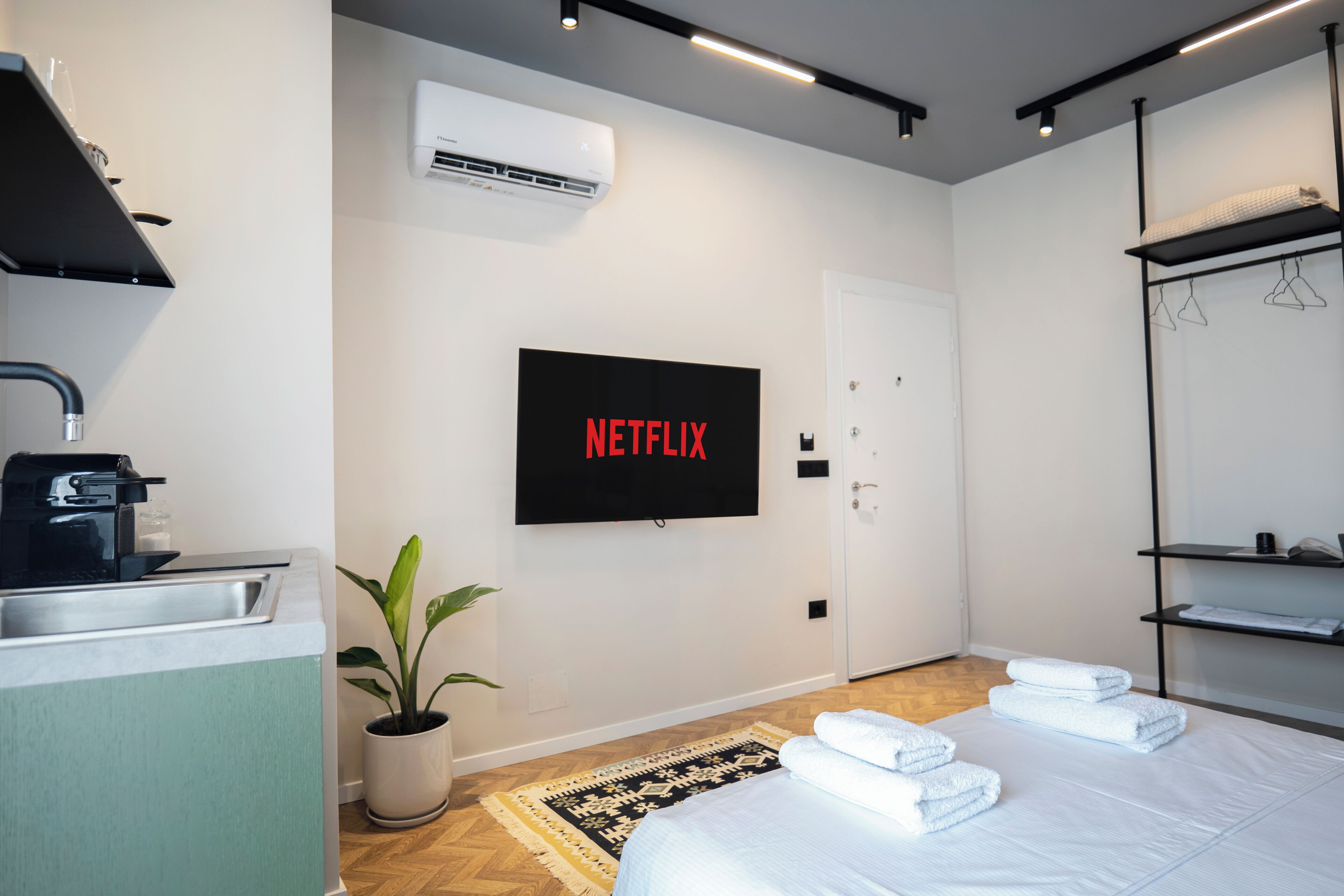 Una moderna camera d'albergo con televisione a schermo piatto, lavandino, una pianta in vaso, un letto con asciugamani e un armadio.