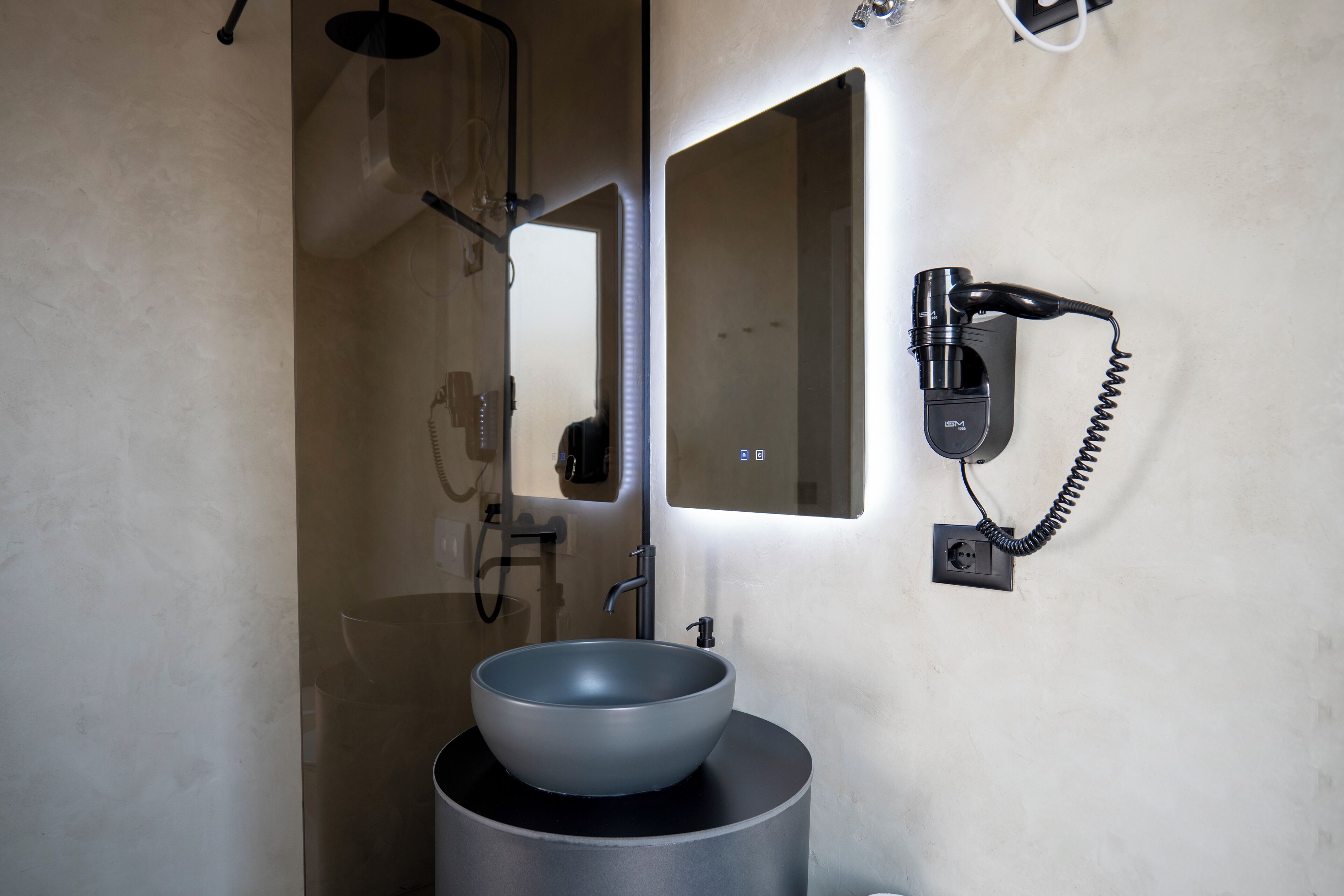 A bathroom with a large mirror, a sink with a bowl, and a hairdryer mounted on the wall.