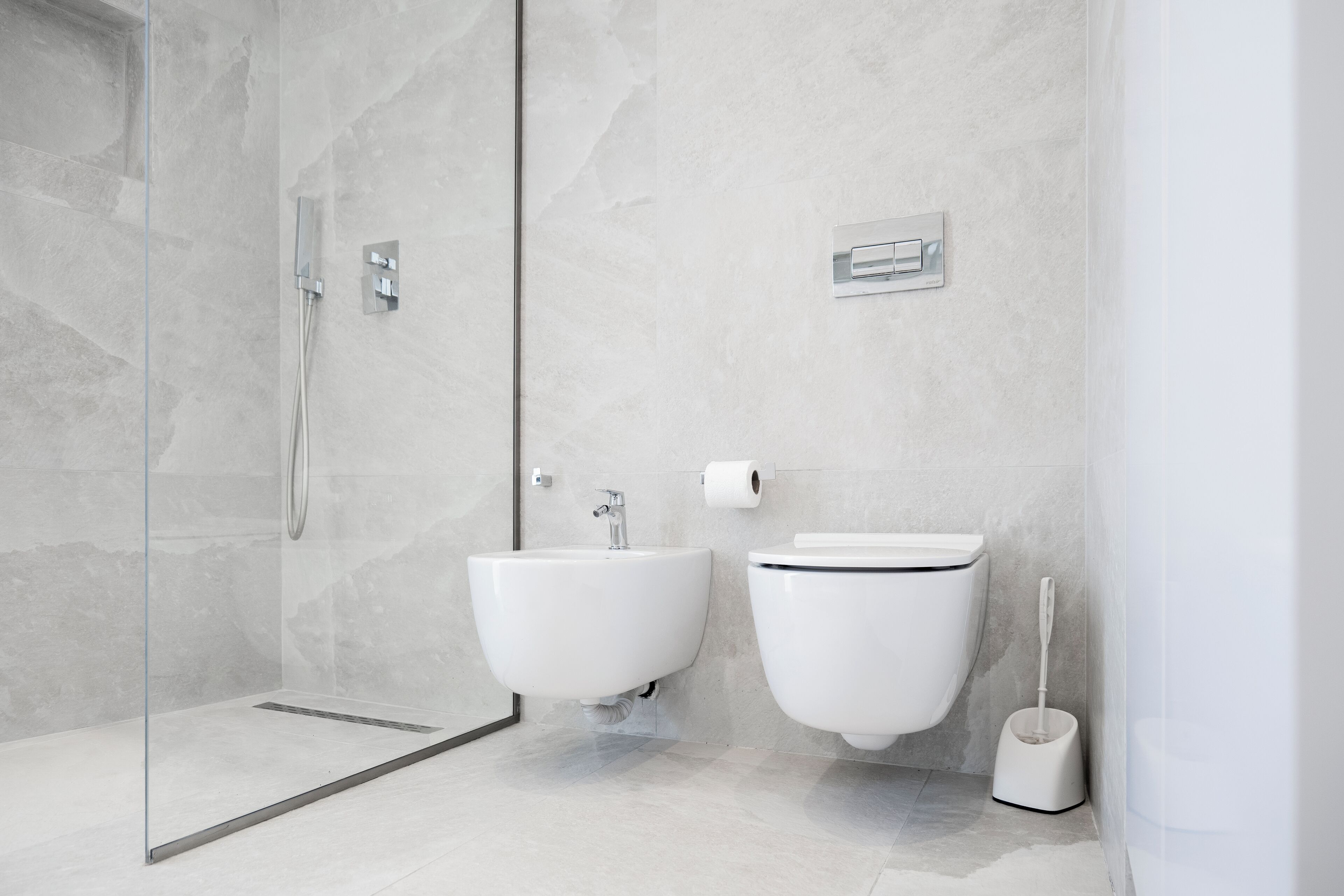 Un bany modern amb plat de dutxa de vidre, un lavabo amb peu i un vàter.