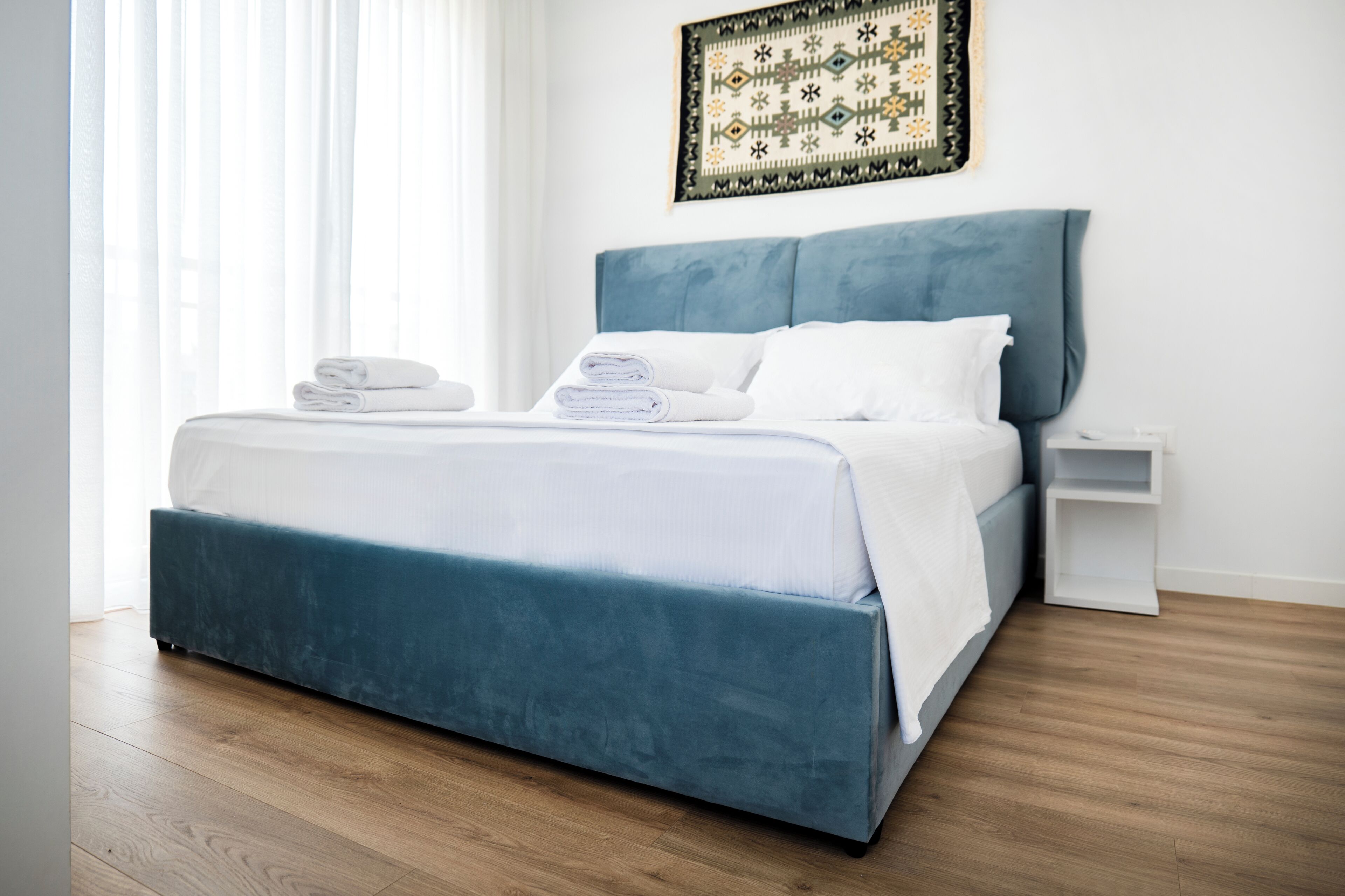 Un dormitorio moderno con una cama grande, toallas blancas dobladas con cuidado y un cabecero azul, sobre un piso de madera.