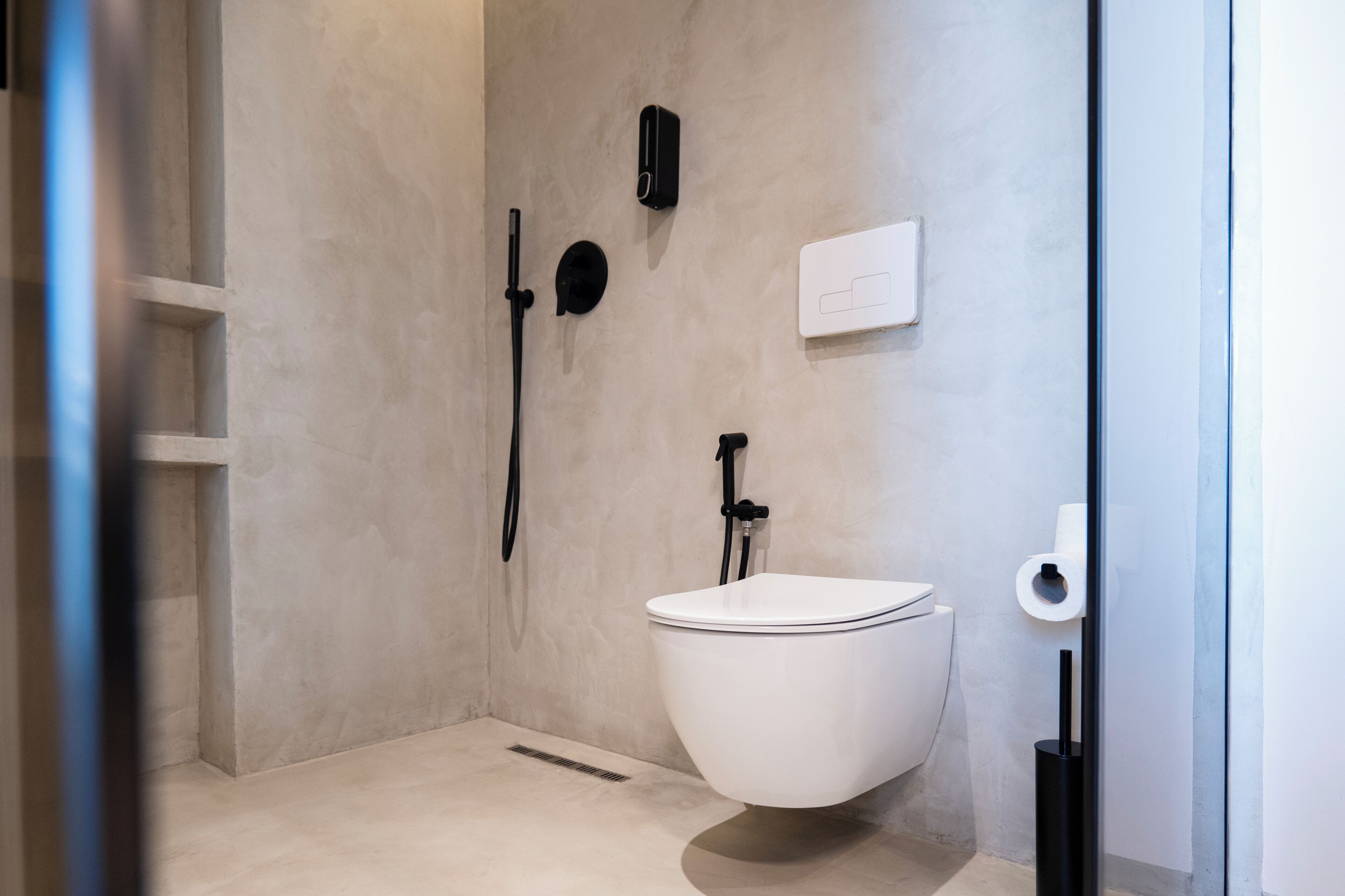 Un baño moderno con inodoro blanco, zona de ducha y dispensador de papel higiénico.