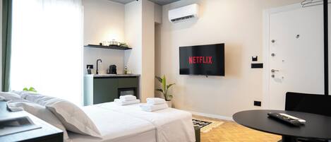 A modern hotel room with a bed, a desk, a chair, a TV, and a small table.