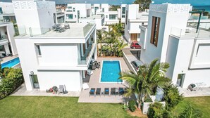 Ein moderner Wohnkomplex mit einem zentralen Schwimmbecken, mehreren Balkonen und üppiger Bepflanzung.