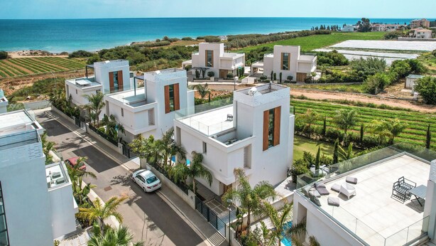 Ein moderner Wohnbereich mit weißen Gebäuden, freiem Blick aufs Meer und einem gepflegten Garten.