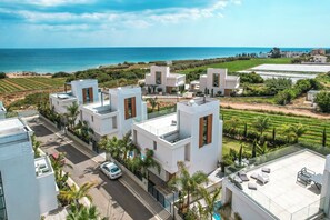 Ein moderner Wohnbereich mit weißen Gebäuden, freiem Blick aufs Meer und einem gepflegten Garten.