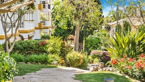 A garden pathway leading to a building with a white facade and yellow accents. - Hacienda Nagueles (Marbella)