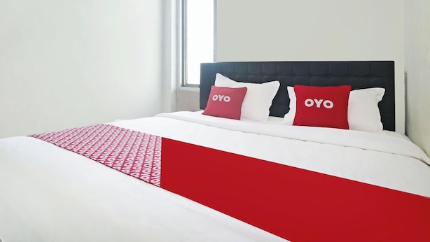 A neatly made bed with a red and white bedspread and two pillows with the word "OYO" on them. - Hotel O Papi Inn Guesthouse (Palangkaraya)