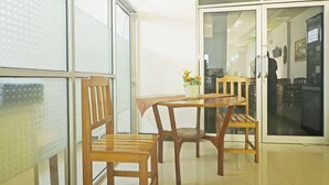 A room with a wooden table and chairs, a window with a view, and a door leading to another room. - Hotel O Papi Inn Guesthouse (Palangkaraya)