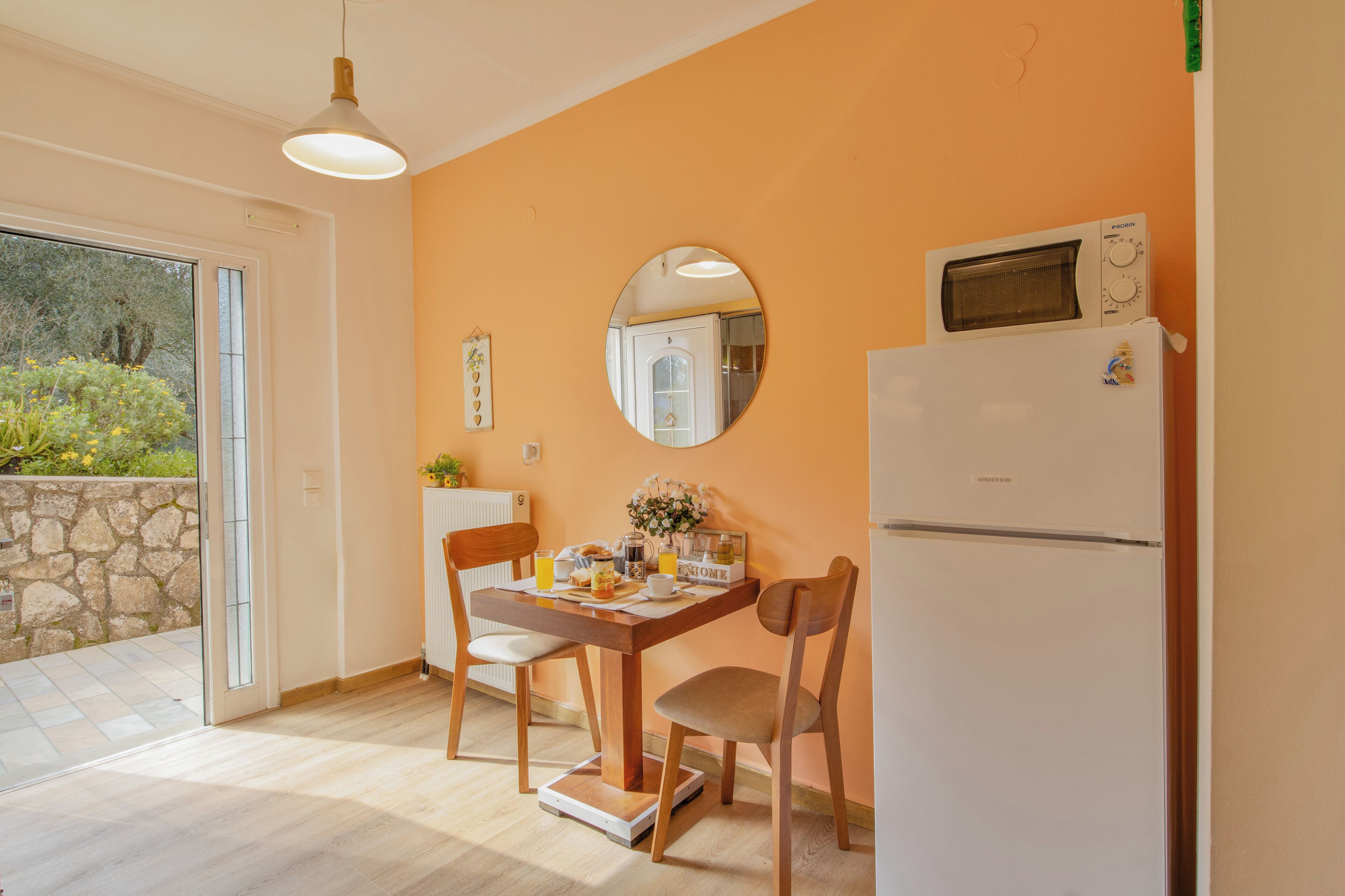 Une cuisine équipée d’une table à manger, de chaises, d’un réfrigérateur, d’un four à micro-ondes et d’une grande fenêtre.