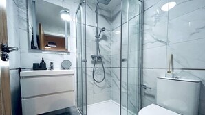 Ein modernes Badezimmer mit einer Duschkabine, einer weißen Toilette und einem Waschtisch mit Spiegel und Ablagefläche.