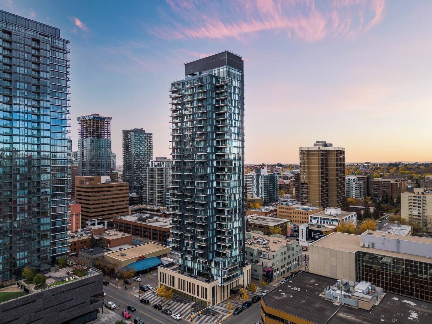 A high-rise building with a modern glass facade, surrounded by other buildings and a clear sky.