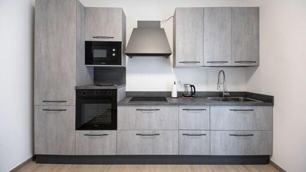 Een moderne keuken met grijze kastjes, een ingebouwde oven, een magnetron, een kookplaat, een spoelbak en een waterkoker.