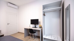Een slaapkamer met een bed, een bureau met een computer, een stoel, een kledingkast en een airconditioning.