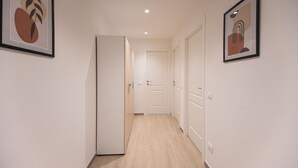 Een gang met een houten vloer, witte muren en deuren die naar kamers leiden. Er hangen kunstwerken in lijsten aan de muren.