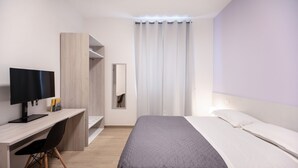 Een moderne hotelkamer met een bed, een bureau met een computer en een kledingkast.