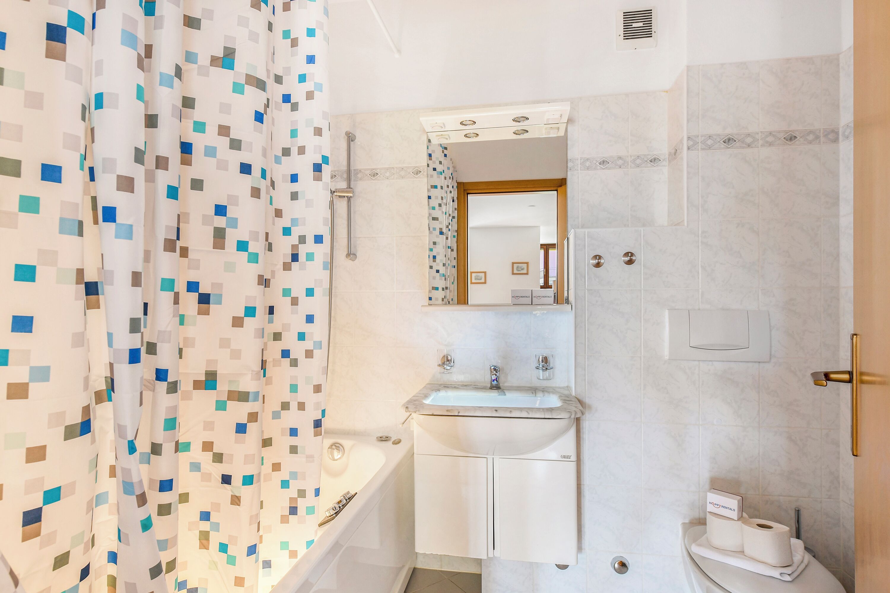 Un baño con cortina de ducha, lavamanos, espejo e inodoro.