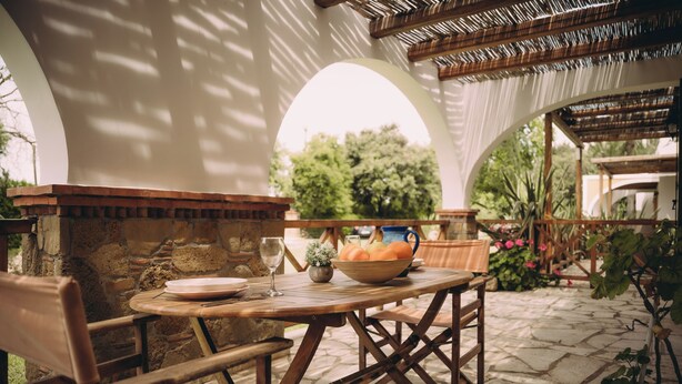 Un patio al aire libre con una mesa redonda de madera, sillas y un bol de fruta.
