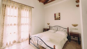 Un dormitorio con cama, cortinas, una mesita de noche, una lámpara de pared y un cuadro pequeño.