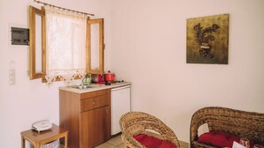 Una cocina compacta con un armario de madera, una olla roja, un lavavajillas blanco y una silla de mimbre con un cojín rojo.