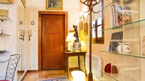A hallway with a wooden door, a glass display case with books, a lamp on a table, and a patterned rug. - Bel Appartement T1bis de Caractère Jardin Royal. Quartier des Carmes (Toulouse)