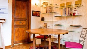 A dining area with a wooden table and chairs, glass shelves with books and decorative items, and a wooden door. - Bel Appartement T1bis de Caractère Jardin Royal. Quartier des Carmes (Toulouse)