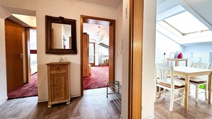 A spacious hallway with wooden flooring, a wooden cabinet, a mirror, and a dining area with a table and chairs. - Calendula vacation apartment (Oberstaufen)