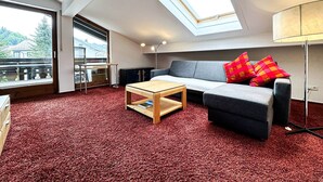 A modern living room with a skylight, a grey sofa with red cushions, a wooden coffee table, and a red carpet. - Calendula vacation apartment (Oberstaufen)