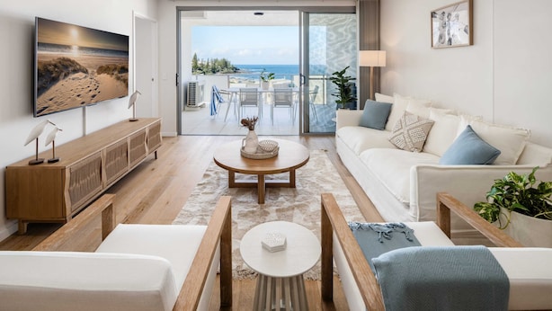 Una sala moderna con un televisor de pantalla plana grande, una consola de madera, un sofá blanco y un comedor con mesa y sillas.