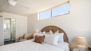 Un dormitorio con cama, mesita de noche, lámpara y ventana.