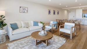 Una sala moderna con un sofá blanco, una mesa de centro de madera y un comedor con sillas de madera.