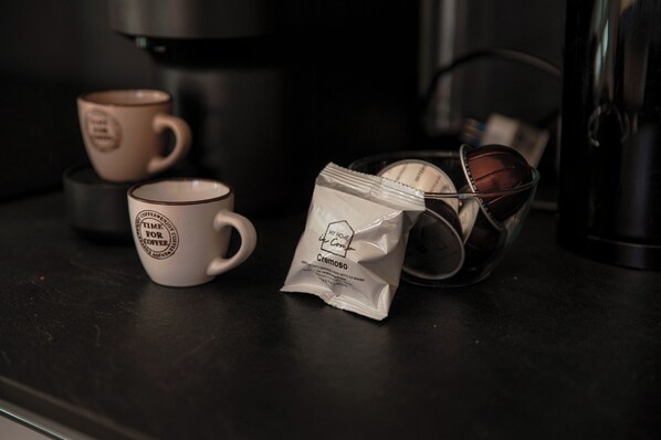 Una preparación para café con dos tazas, una cafetera y un sobre de leche condensada sobre una encimera oscura.