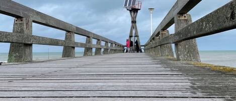 A wooden pier leading to a lighthouse structure with a person standing at the end.