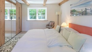 Un dormitorio con una cama grande, una silla, una lámpara y una ventana con vistas a la vegetación.