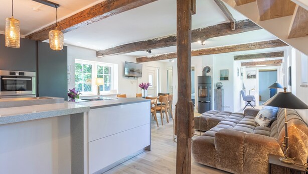 Una cocina moderna con una isla central, vigas de madera y una sala de estar acogedora con sofá y lámpara.