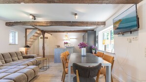 Una sala de estar moderna con un sofá, una mesa de comedor y sillas. Se observa un área de cocina al fondo y una escalera que conduce a otro nivel.
