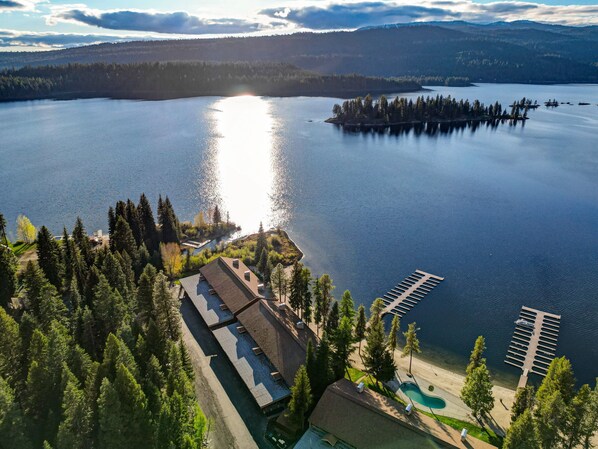 Vue aérienne d’une propriété au bord du lac, avec une piscine, un quai et une zone boisée.