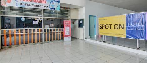 A hotel lobby with a reception desk, a sign for 'Area Wajib Vaksin & Pakai Masker', and a 'Spot On Hotel Margadana' sign.
